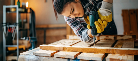 Woman using power drill to put a screw into a piece of wood